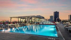 Optima Lakeview® Apartments in Chicago, IL Rooftop swimming pool at sunset with city buildings in the background and lounge chairs beside the pool.