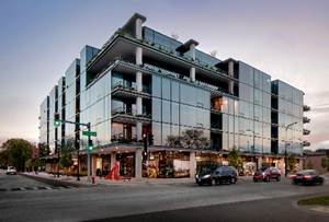 Optima Lakeview® Apartments in Chicago, IL Modern glass building with street-level shops, cars passing by, and people walking—creating a vibrant home environment at dusk.