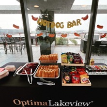 Optima Lakeview® Apartments in Chicago, IL A table labeled "Hotdog Bar" holds hot dogs, buns, chips, and condiments by large windows with a patio view.