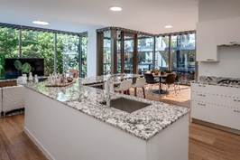 Optima Lakeview® Apartments in Chicago, IL Modern kitchen with a granite island, sink, and large windows overlooking a dining area and greenery.
