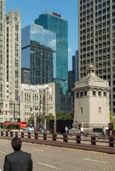 Optima Lakeview® Apartments in Chicago, IL A man stands on a city bridge, enjoying a short commute between modern skyscrapers and historic buildings on a sunny day.