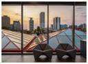 Optima Lakeview® Apartments in Chicago, IL Two modern chairs by large windows overlook city buildings and a glass roof at sunset.