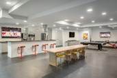 Optima Lakeview® Apartments in Chicago, IL Modern game room with a long table, bar area, TV screens, and a pool table under bright ceiling lights.