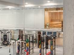 Optima Lakeview® Apartments in Chicago, IL Modern gym interior with exercise equipment on the lower level and a wooden sauna room visible on the upper level behind glass walls.