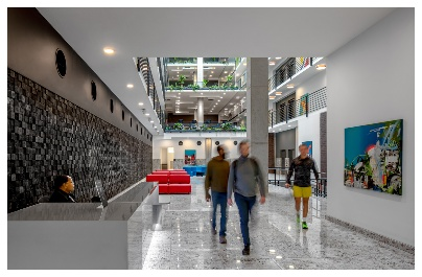 Optima Lakeview® Apartments in Chicago, IL Four people stroll through Optima Lakeview’s modern lobby, with red seating, art, and leafy plants on upper balconies.