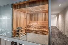 Optima Lakeview® Apartments in Chicago, IL A modern wooden sauna with tiered benches behind a glass wall, next to a hallway with gray carpet and lighting.