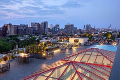 Optima Lakeview® Apartments in Chicago, IL Rooftop with seating, a pool, and city skyline in the background at sunset.